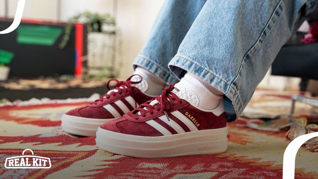 Someone in white socks and light blue jeans wearing a pair of dark red and white adidas Gazelles with chunky midsoles.