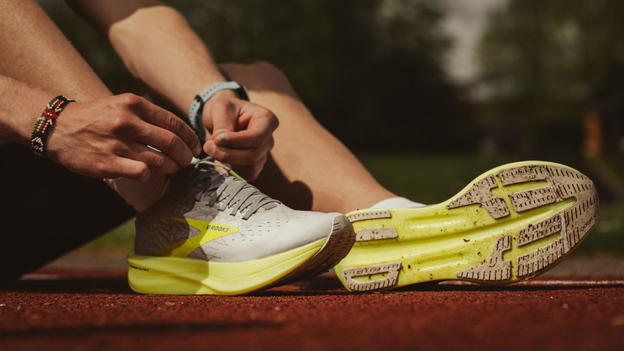 A person tying up a grey and yellow running shoe while sat on a running track.